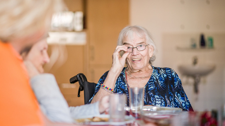 lachende Seniorin an Tisch - Immanuel Ambulante Schmalkalden-Meiningen - Angebot